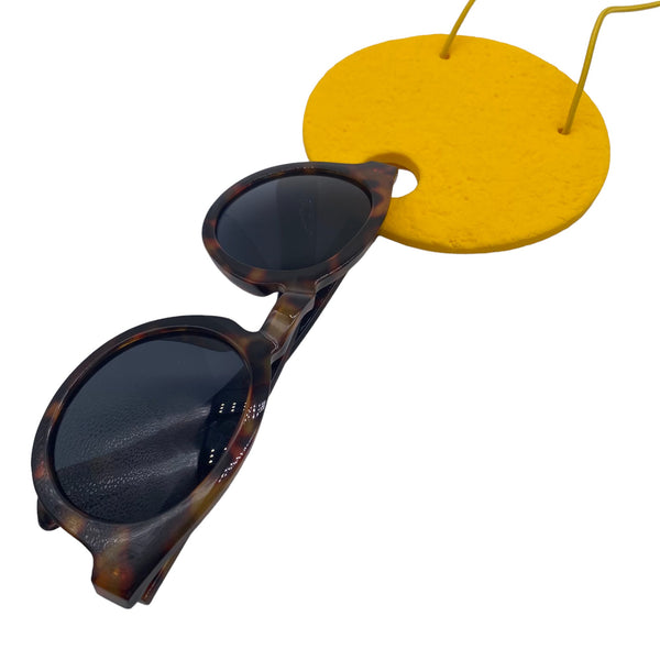Large yellow Polymer Clay Statement necklace holding sunglasses on a white background